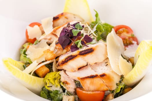Fresh delicious caesarsalat with grilled chicken bust parmesan shards and croutons isolated against a white background