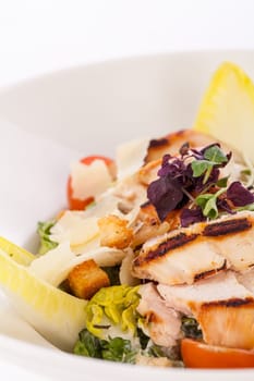 Fresh delicious caesarsalat with grilled chicken bust parmesan shards and croutons isolated against a white background