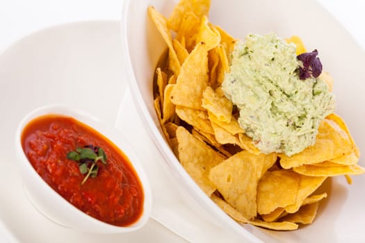 Corn chips nachos with guacamole and salsa dipp in a bowl on a plate insulated against a white background