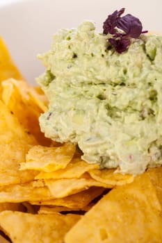Corn chips nachos with guacamole and salsa dipp in a bowl on a plate insulated against a white background