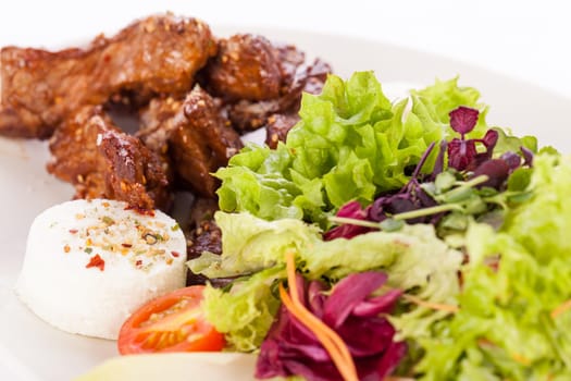 Fresh salad with fresh goat cheese and fried beef strips prepared on a plate insulated against a white background
