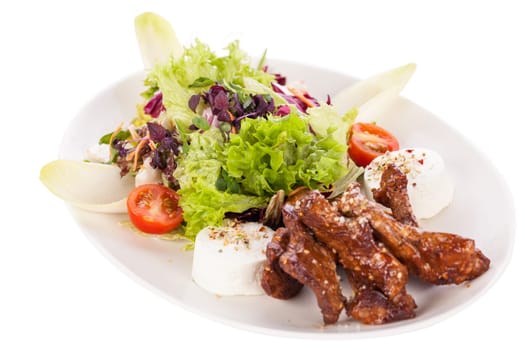 Fresh salad with fresh goat cheese and fried beef strips prepared on a plate insulated against a white background