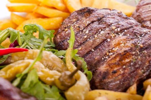 Huge barbecue plate with mixed meat and steaks on salad isolated against a white background