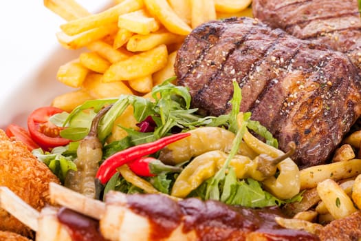 Huge barbecue plate with mixed meat and steaks on salad isolated against a white background