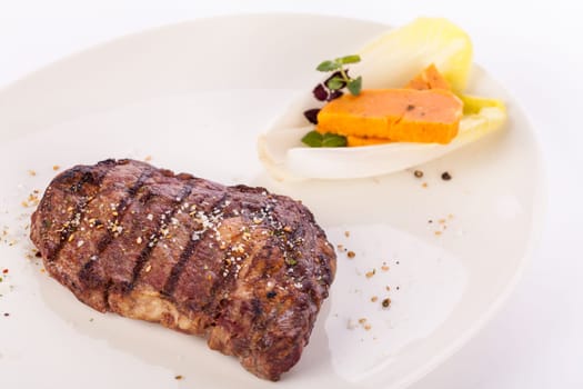 Succulent grilled beef fillet steak with homemade herb butter on a plate isolated against a white background