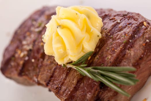 Succulent grilled beef fillet steak with homemade herb butter on a plate isolated against a white background