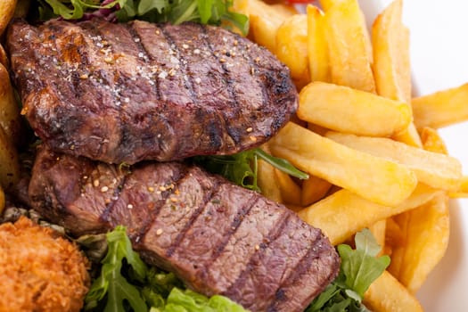 Huge barbecue plate with mixed meat and steaks on salad isolated against a white background