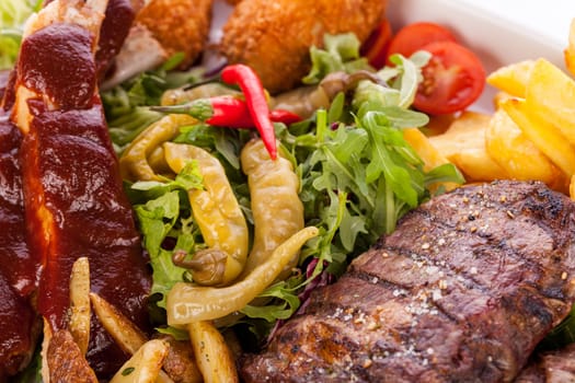 Huge barbecue plate with mixed meat and steaks on salad isolated against a white background
