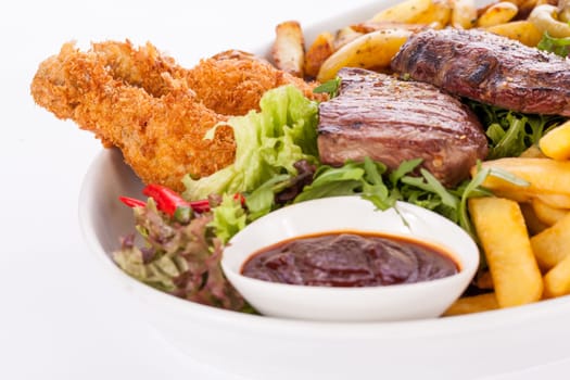 Huge barbecue plate with mixed meat and steaks on salad isolated against a white background