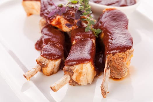 Grilled pork ribs Spareribs with barbecue sauce marinade and herb salad on a plate isolated against a white background