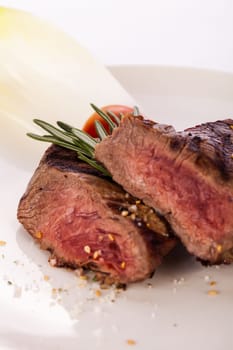 Medium fried beef steak fillet with pepper and rosemary sliced on a plate insulated against white background
