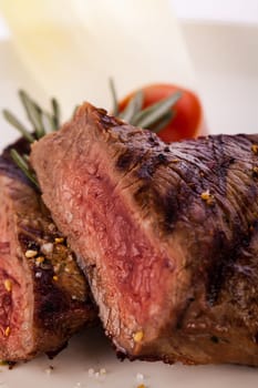 Medium fried beef steak fillet with pepper and rosemary sliced on a plate insulated against white background