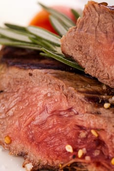 Medium fried beef steak fillet with pepper and rosemary sliced on a plate insulated against white background