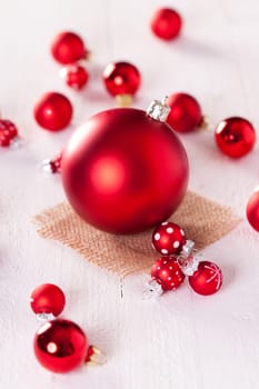 large and small red Christmas tree balls on a wooden board with a jutesack as a close-up