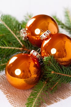 Shiny orange glass balls Christmas balls with green twigs on a jute sack as a close-up