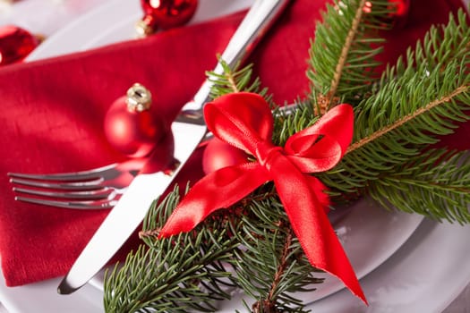 Red napkin with Christmas glass balls and cutlery with a green fir branch and red bow close-up