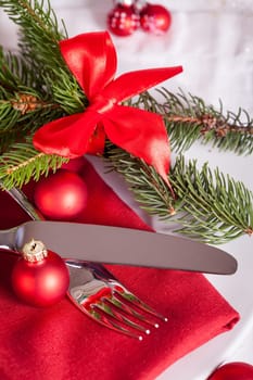 Red napkin with Christmas glass balls and cutlery with a green fir branch and red bow close-up