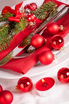 Red napkin with Christmas glass balls and cutlery with a green fir branch and red bow close-up