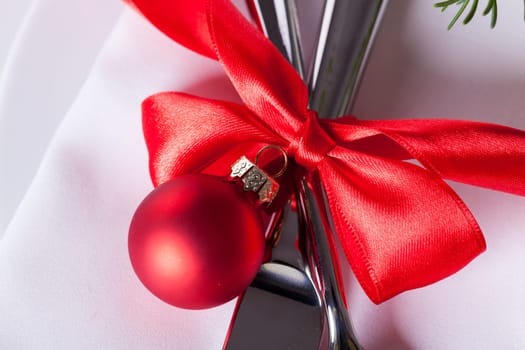 Romantic Christmas table with red balls and red bow with cutlery knife and fork on a napkin