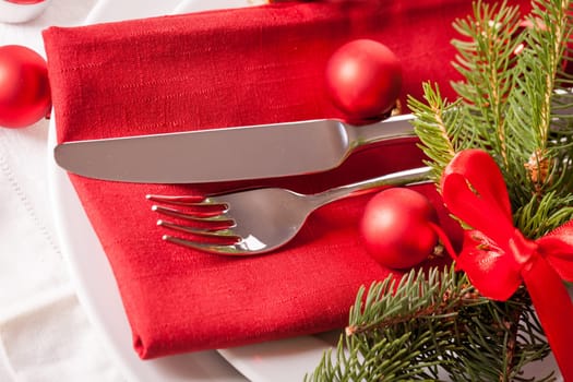 Red napkin with Christmas glass balls and cutlery with a green fir branch and red bow close-up