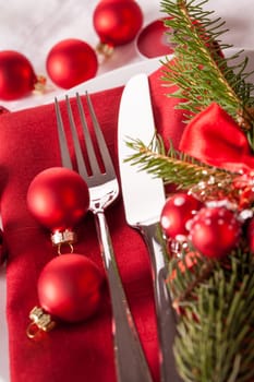 Red napkin with Christmas glass balls and cutlery with a green fir branch and red bow close-up