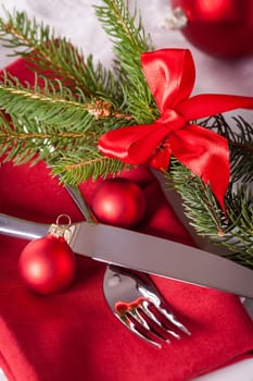 Red napkin with Christmas glass balls and cutlery with a green fir branch and red bow close-up