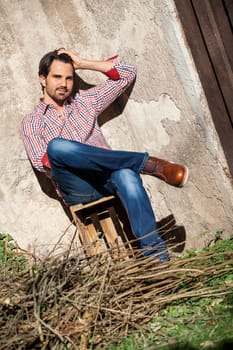 Young man with a plaid shirt and jeans with dark hair and beard outdoors under an efeuranke in daylight