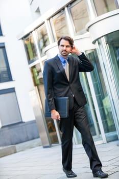 Young trendy businessman in front of a business building successfully with beard and dark hair