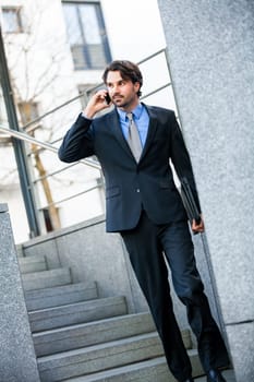 Young trendy successful businessman with mobile phone smartphone cheerful lyrane in front of an outdoor business building