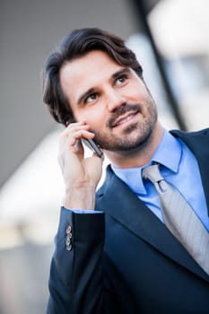 Young trendy successful businessman with mobile phone smartphone cheerful lyrane in front of an outdoor business building