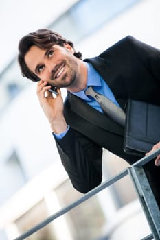 Young trendy successful businessman with mobile phone smartphone cheerful lyrane in front of an outdoor business building