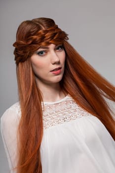 Young attractive female girl with long red hair in portrait against grey background