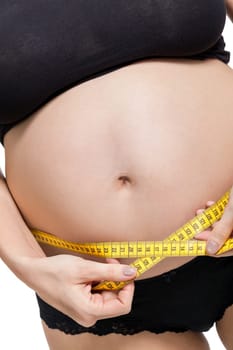 Pregnant woman with a measuring tape measures her girth on her abdomen isolated against a white background