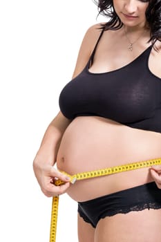 Pregnant woman with a measuring tape measures her girth on her abdomen isolated against a white background