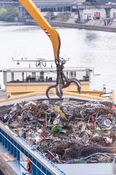 Truck crane with scrap metal loads a cargo ship at the dock with scrap
