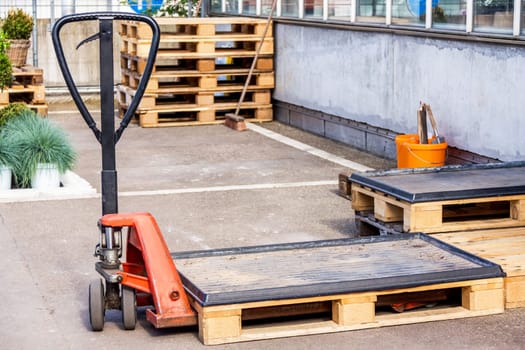 Small orange forklift in front of a warehouse with many pallets in daylight