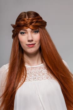 Young attractive female girl with long red hair in portrait against grey background