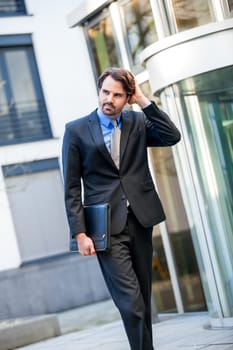 Young trendy businessman in front of a business building successfully with beard and dark hair