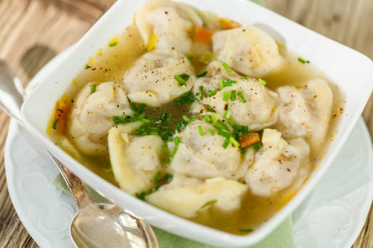 Bowl with Russian Pelmeni Italian tortellini with broth and parsley close-up on a wooden table