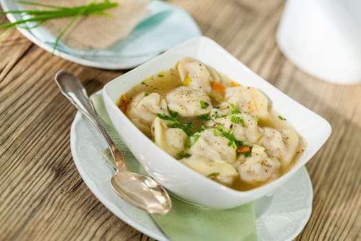 Bowl with Russian Pelmeni Italian tortellini with broth and parsley close-up on a wooden table