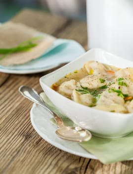 Bowl with Russian Pelmeni Italian tortellini with broth and parsley close-up on a wooden table