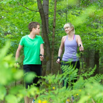 Young spoty active cople with hiking sticks walking in nature. Active lifestyle. Activities and recreation outdoors.