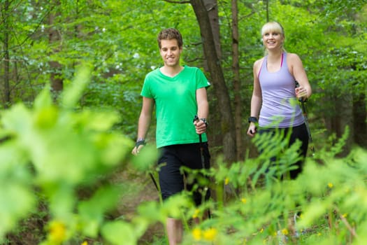 Young spoty active cople with hiking sticks walking in nature. Active lifestyle. Activities and recreation outdoors.