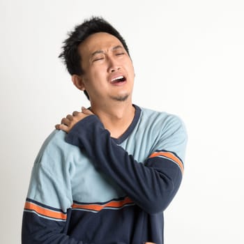 Asian man neck muscle sprain, or shoulder pain, on plain background.