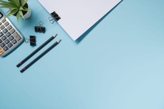 Top view of blank notebook, pen, calculator and green plant on blue office desk