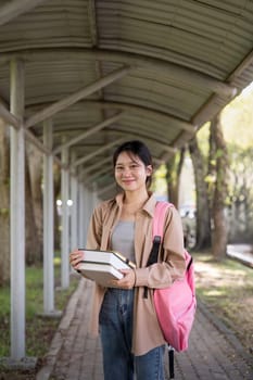 Beautiful young woman asian with backpack and book. College student carrying lots of books in college campus.