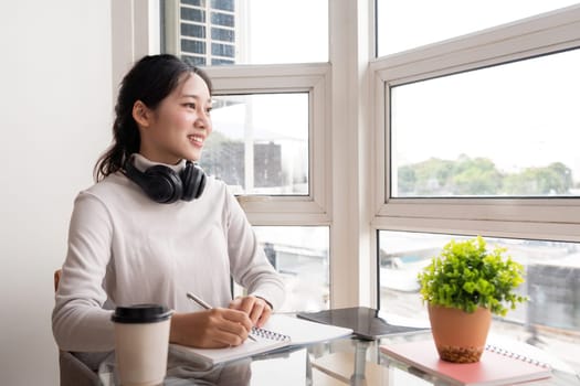 Beautiful young asian woman sitting and taking note on the desk at house. Happy smiling working online, Freelance work at home.