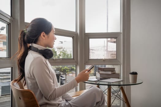 Happy woman asian relax holding smartphone in hands. Smiling young lady chatting in social networks, watching funny video, using mobile application at home.