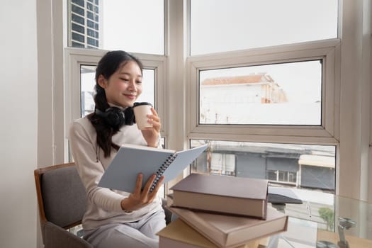 Young beautiful woman asian holding coffee and read a book while relax during work at home.