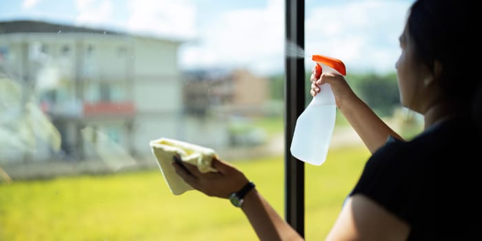 Young Asian housewife cleaning window glass with rags and detergent spray, cleaning house on the weekend.